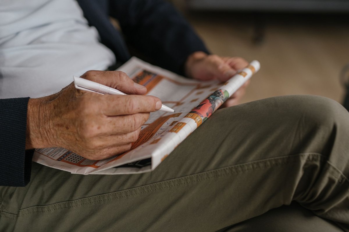 Hands of an older person filling in a newspaper crossword puzzle with a pen