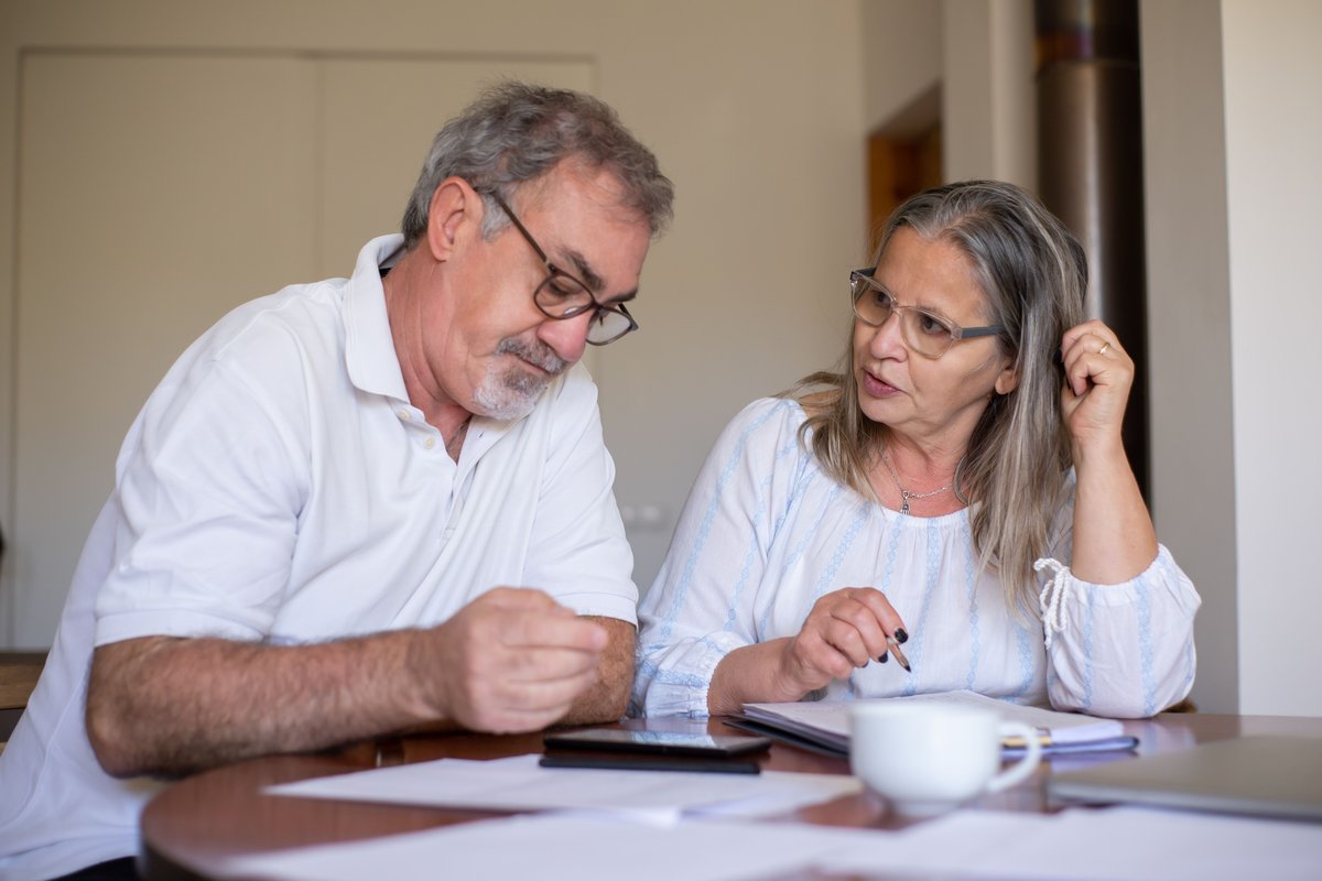 Older couple talking over papers and a phone at a table at home
