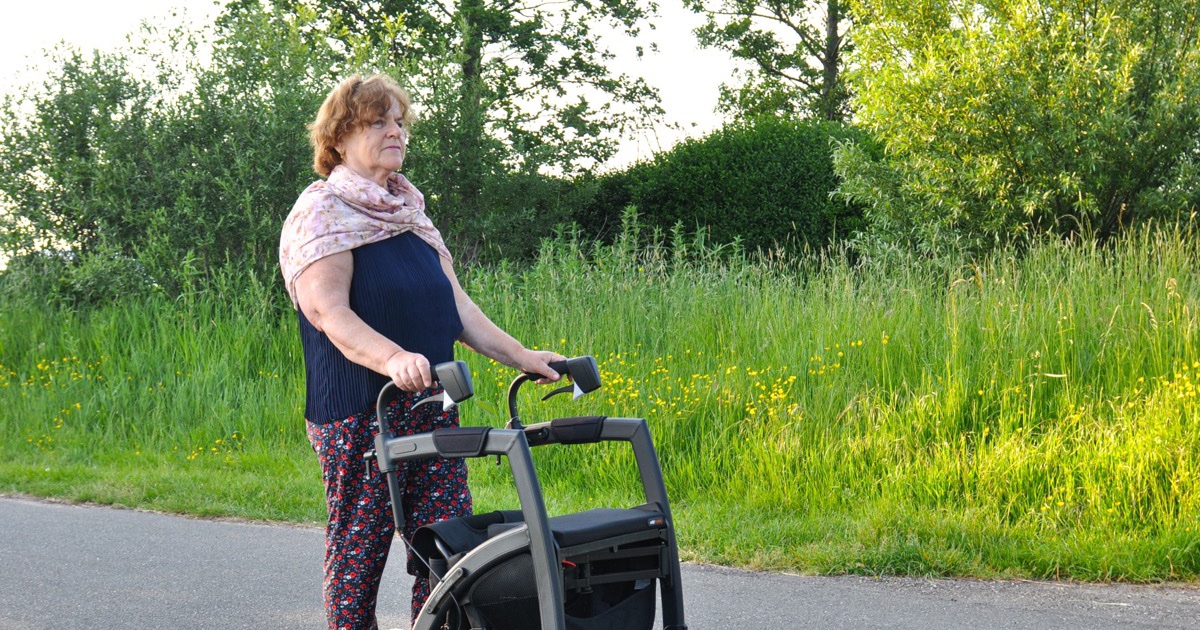Older woman with a rollator walker standing on a sunny country road