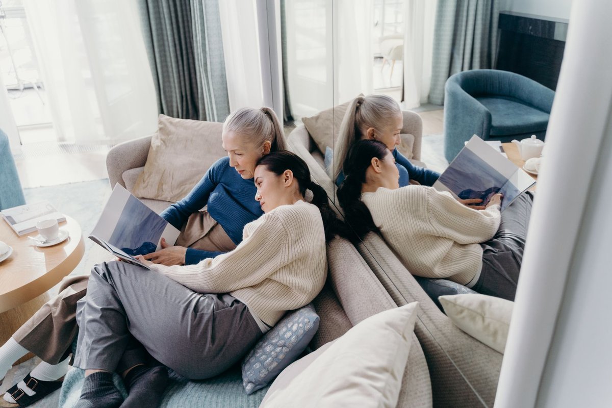 Two women relaxing on a sofa reading magazines together in a bright living room