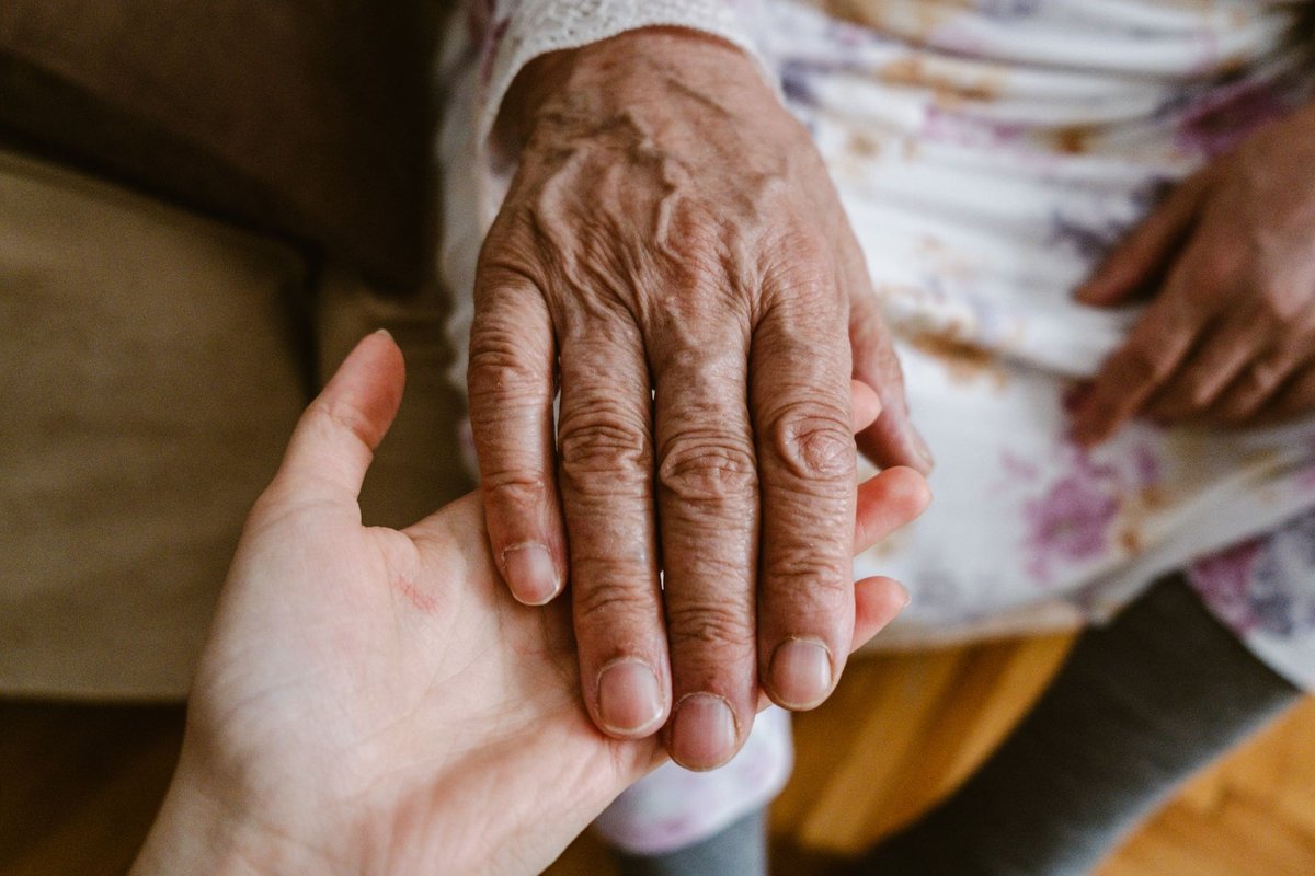 Young person's hand gently holding the hand of an older person