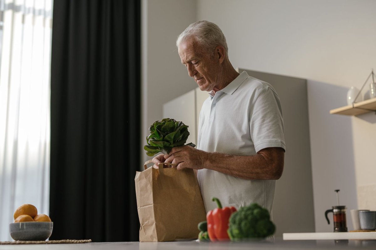 Older man taking fresh lettuce from a paper grocery bag in his kitchen