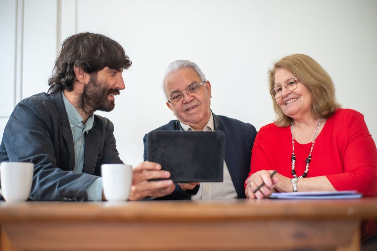 Older couple smiling as an adviser shows them information on a tablet at a table