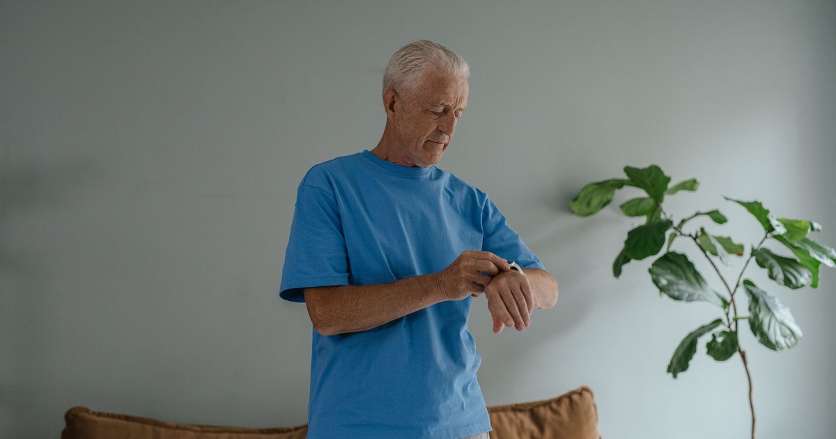 Older man in a blue shirt standing at home and touching the wristband on his wrist