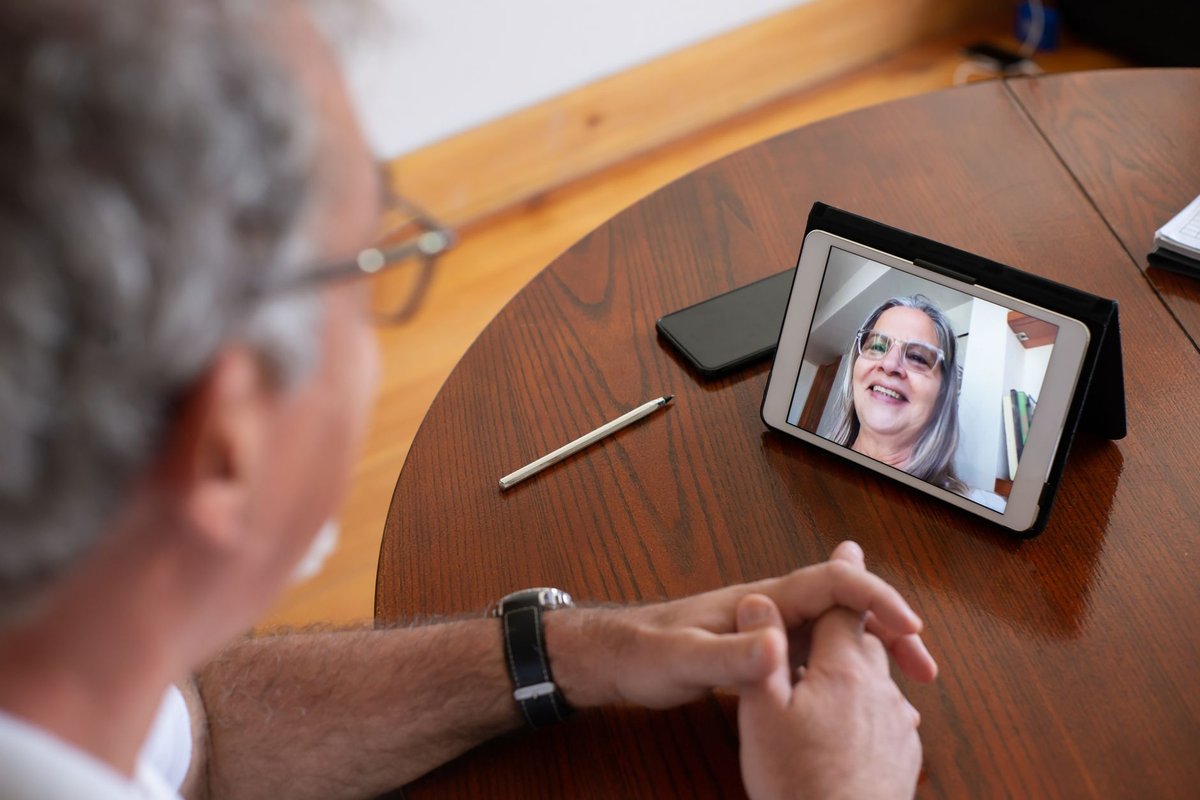 Older man at a wooden table on a video call with a smiling woman on a tablet