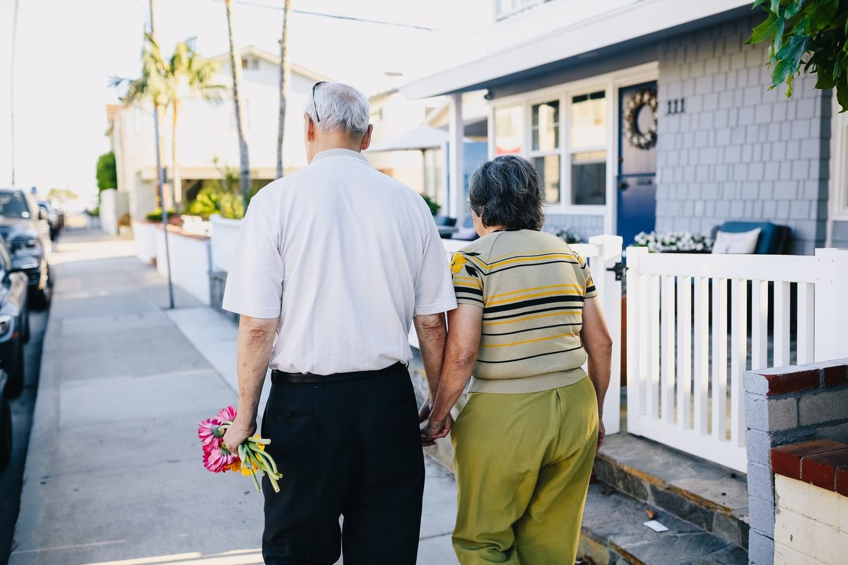 Older couple holding hands while walking along a sunny residential street