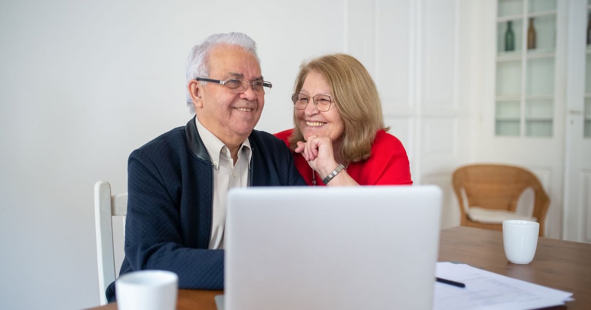 Smiling older couple sitting at a table with a laptop and papers at home