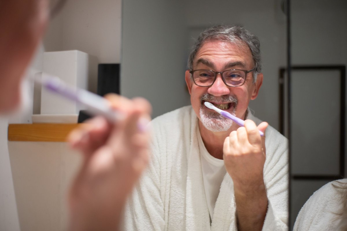 Man with glasses brushing his teeth in front of a bathroom mirror