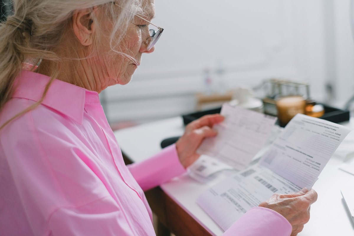 Older woman in a pink shirt reading benefit papers at a table