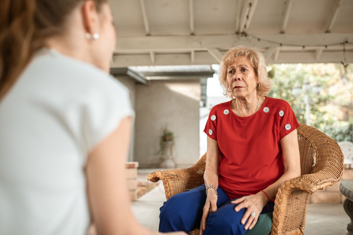 Older woman in a red top leaning forward to listen closely to a younger woman