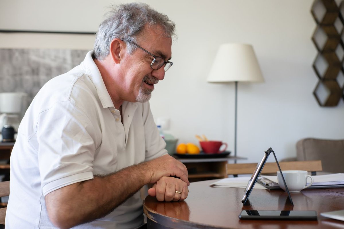 Smiling older man with glasses chatting on a video call at his dining table