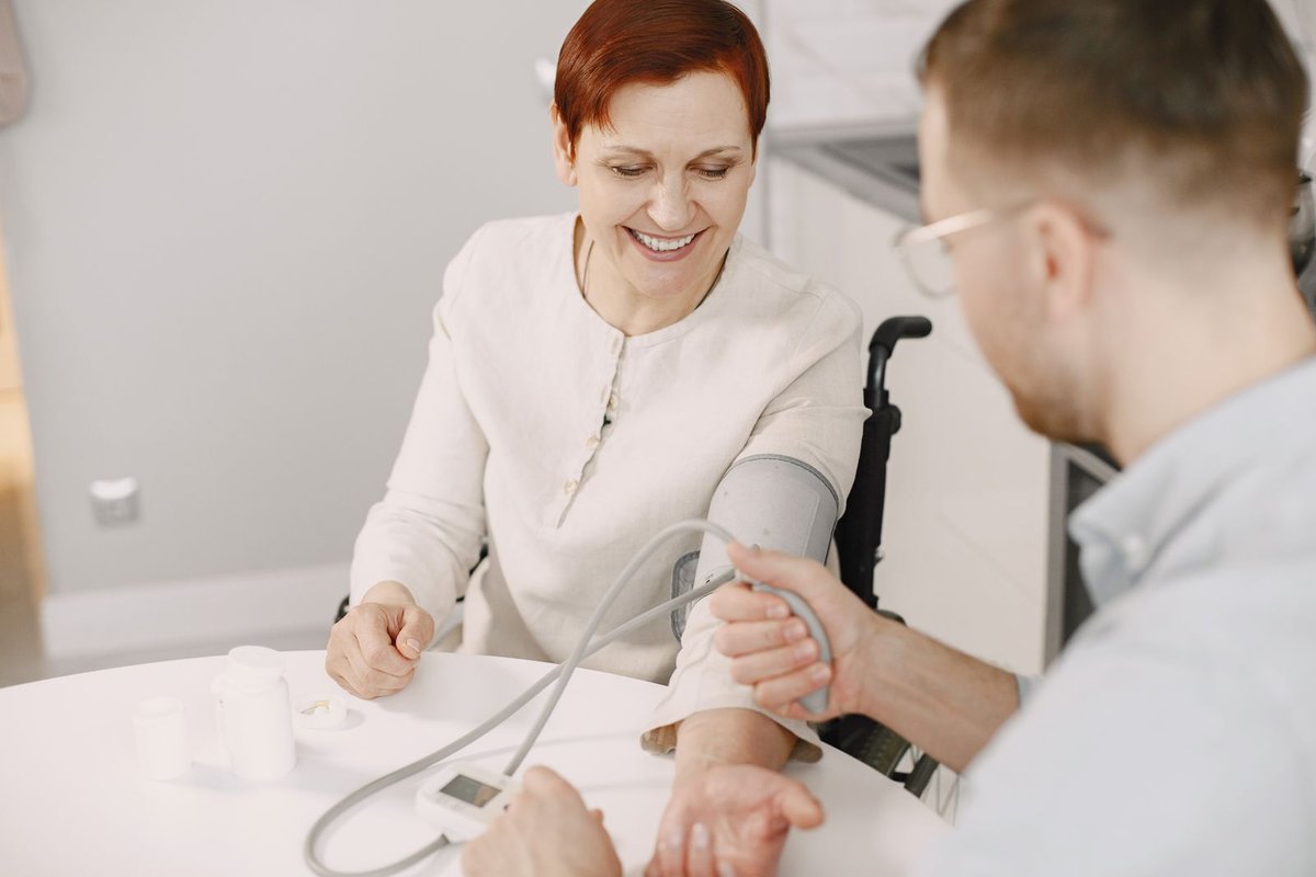 Smiling woman at a table having her blood pressure checked by a visiting helper
