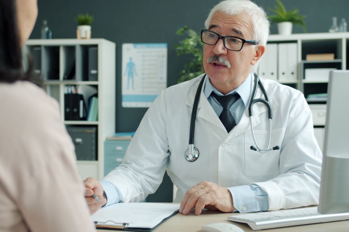 Doctor in a white coat talking with a patient across a desk in a bright office