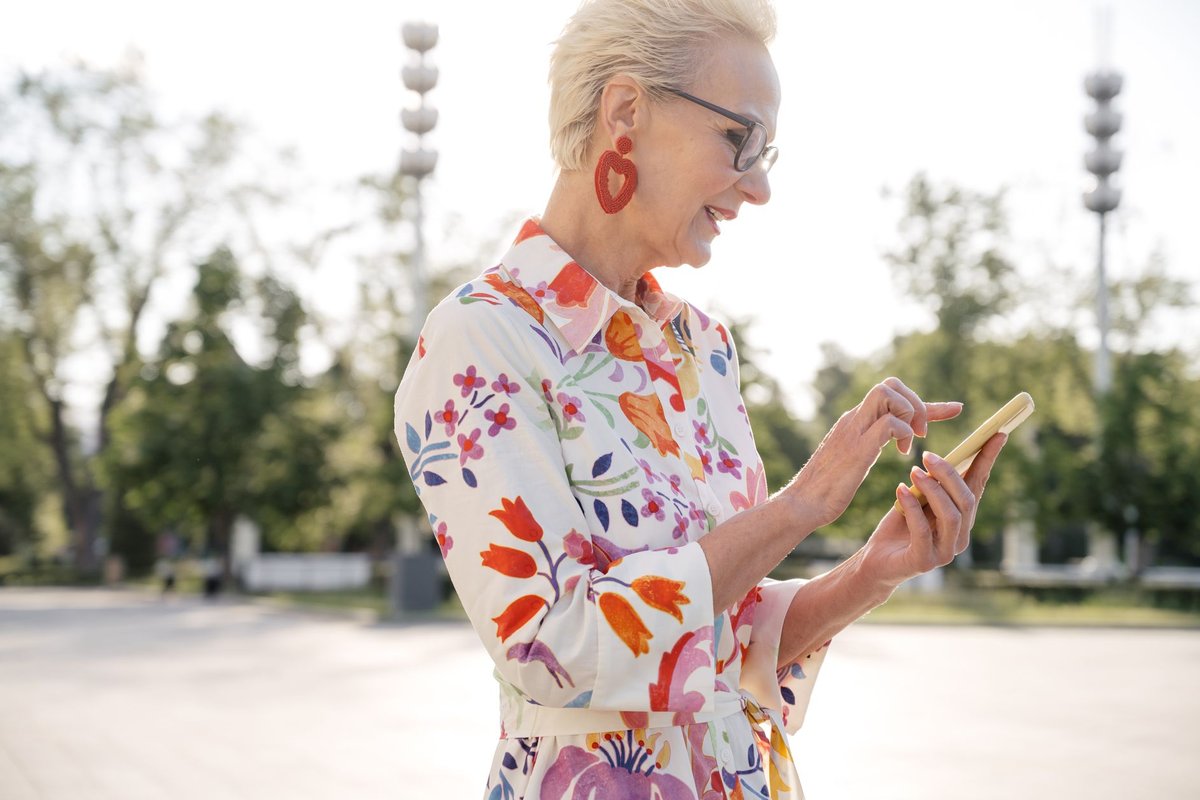 Smiling older woman with short blond hair using her smartphone outdoors on a sunny day