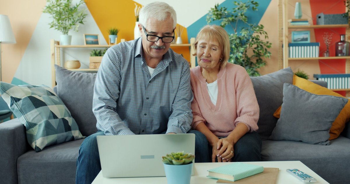 Senior couple sitting on a sofa looking at a laptop together in a bright living room