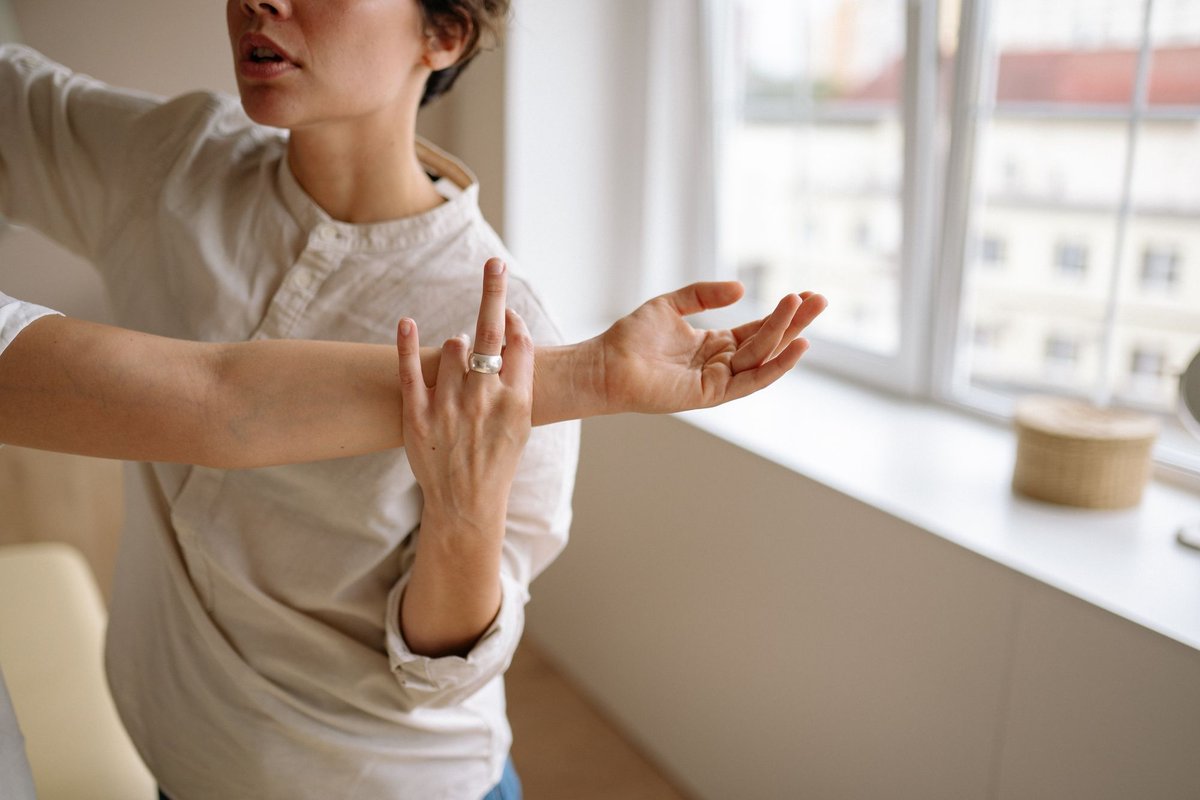 Physical therapist's hands guiding a client's outstretched arm beside a bright window