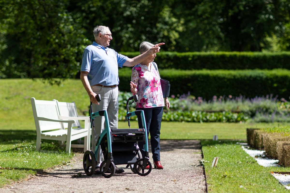 Older couple with a rollator walker pausing on a garden path on a sunny day