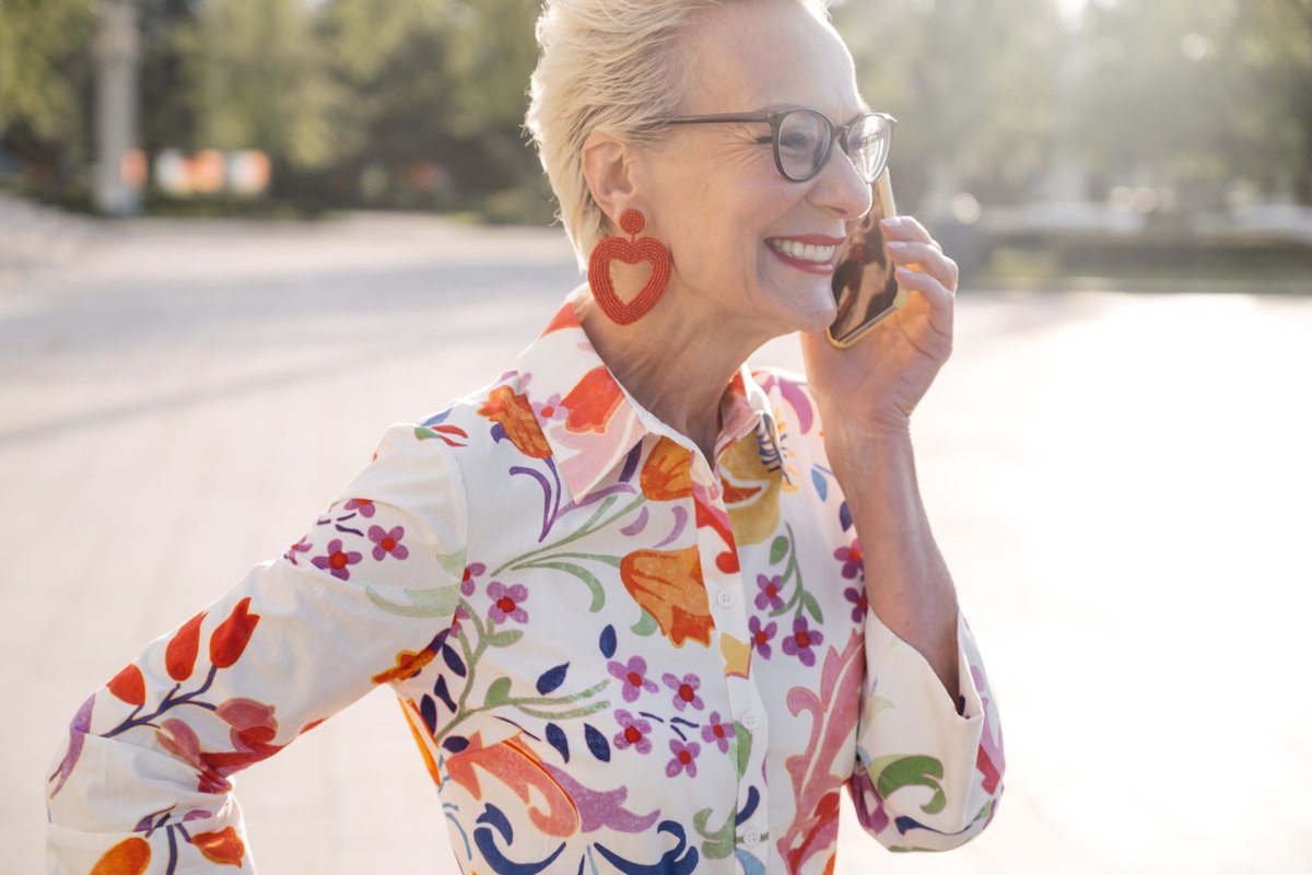 Smiling older woman with short blond hair talking on her phone outdoors in the sun