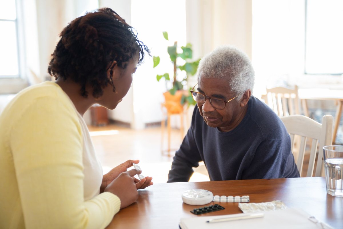 A woman sitting at a table with an older man going over his medications