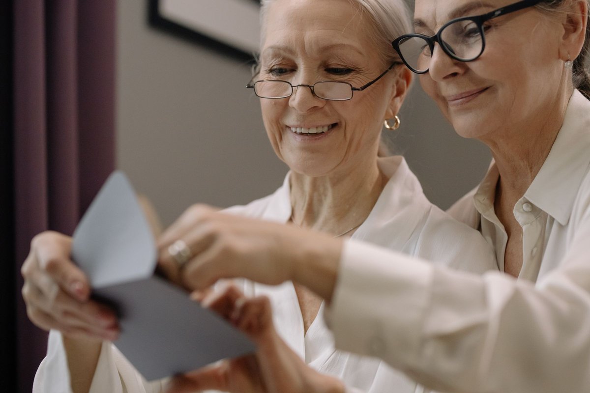 Two older women with glasses smiling as they read a letter together
