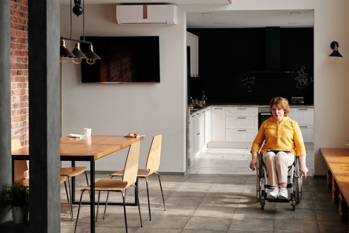Woman in a wheelchair moving through a bright open kitchen and dining area at home