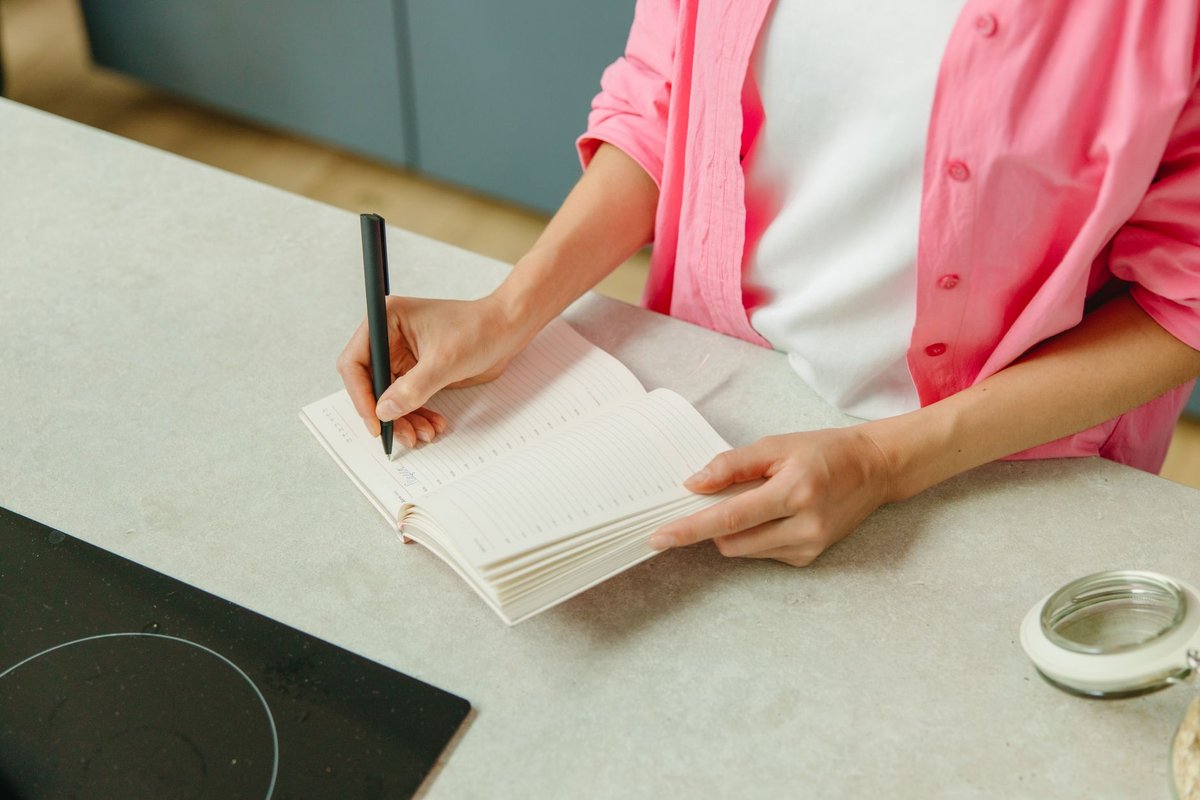 Woman writing in an open notebook at a kitchen counter