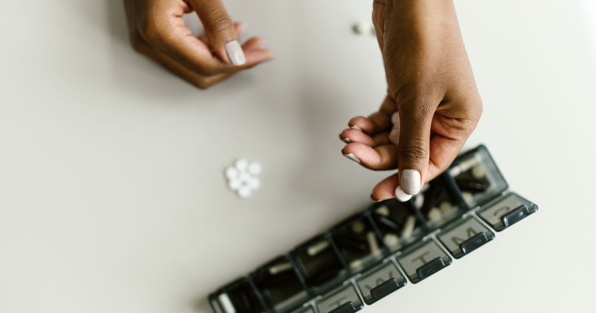 Hands sorting tablets into a weekly pill organizer on a light table