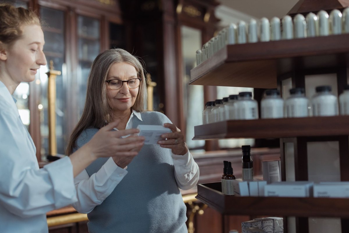 Older woman and a pharmacist looking together at a medicine box in a pharmacy
