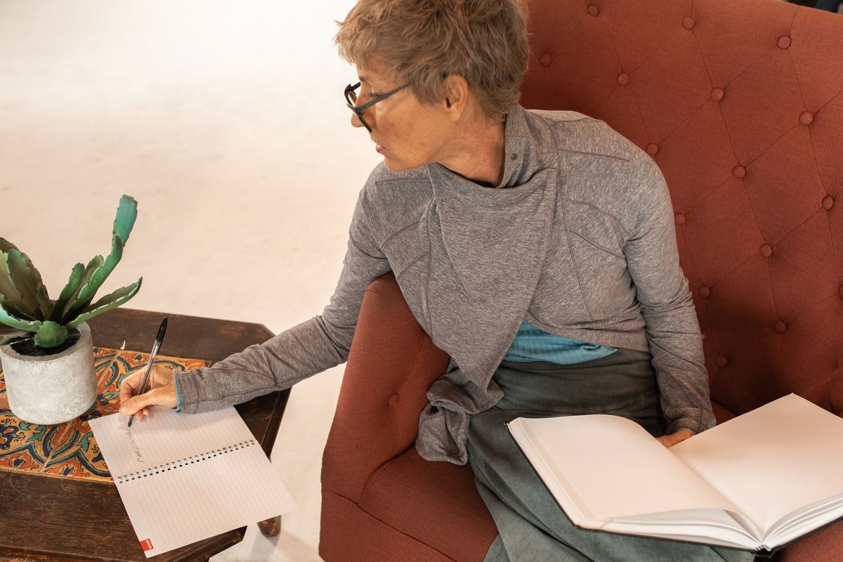 Older woman in an armchair writing a list in a notebook