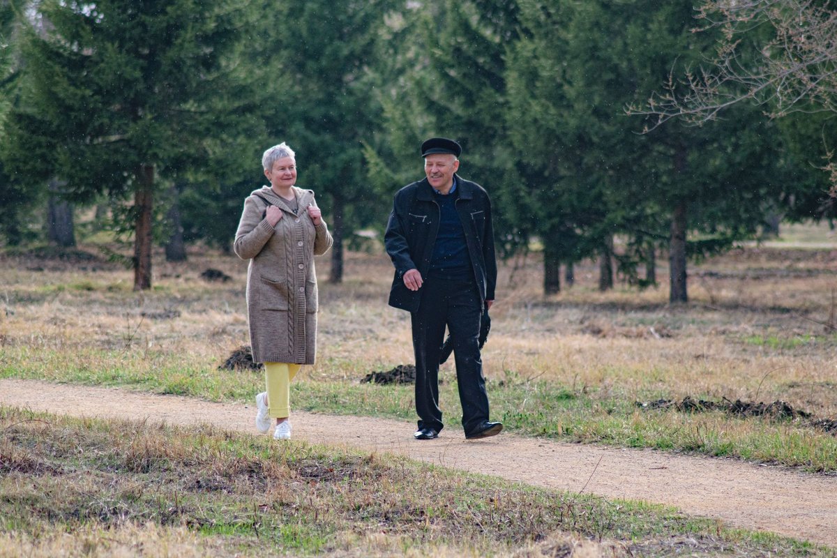Older couple in coats walking together along a park path between trees
