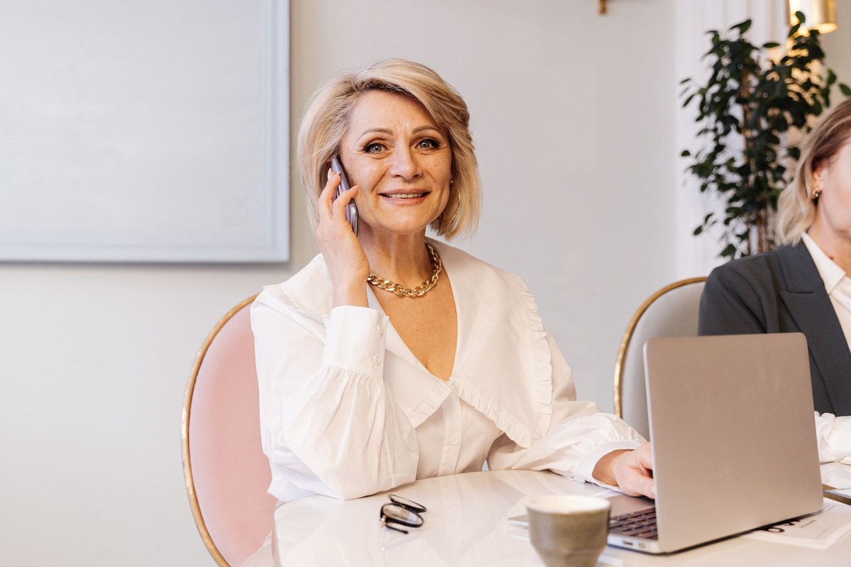 Smiling woman on a phone call sitting at a table with an open laptop