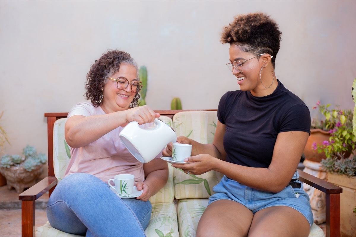 Two women of different generations smiling and pouring tea together on a garden bench