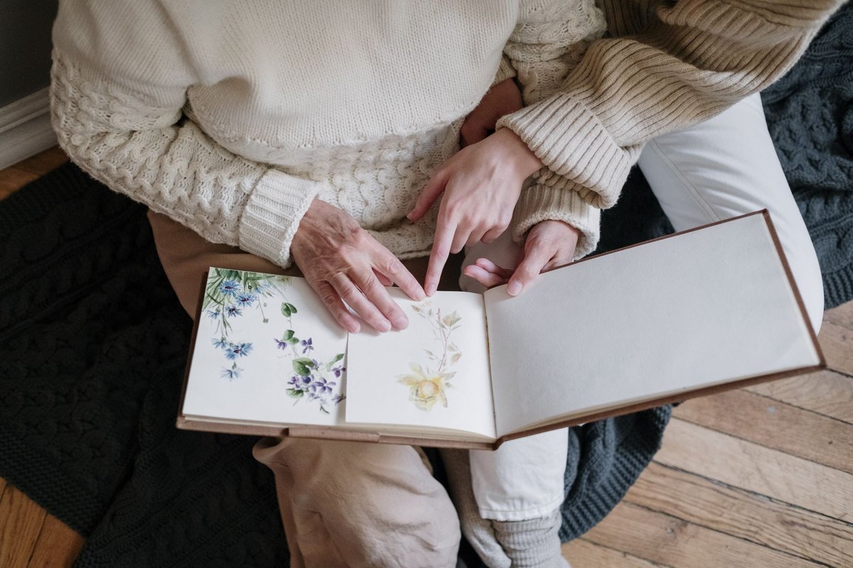 Hands of an older person and an adult looking together at a flower illustrated album