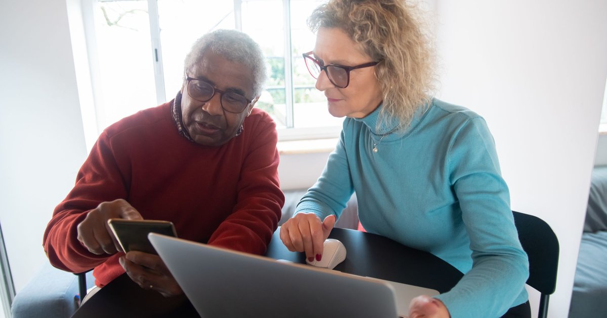 Older man and a woman looking at a laptop and phone together at a table