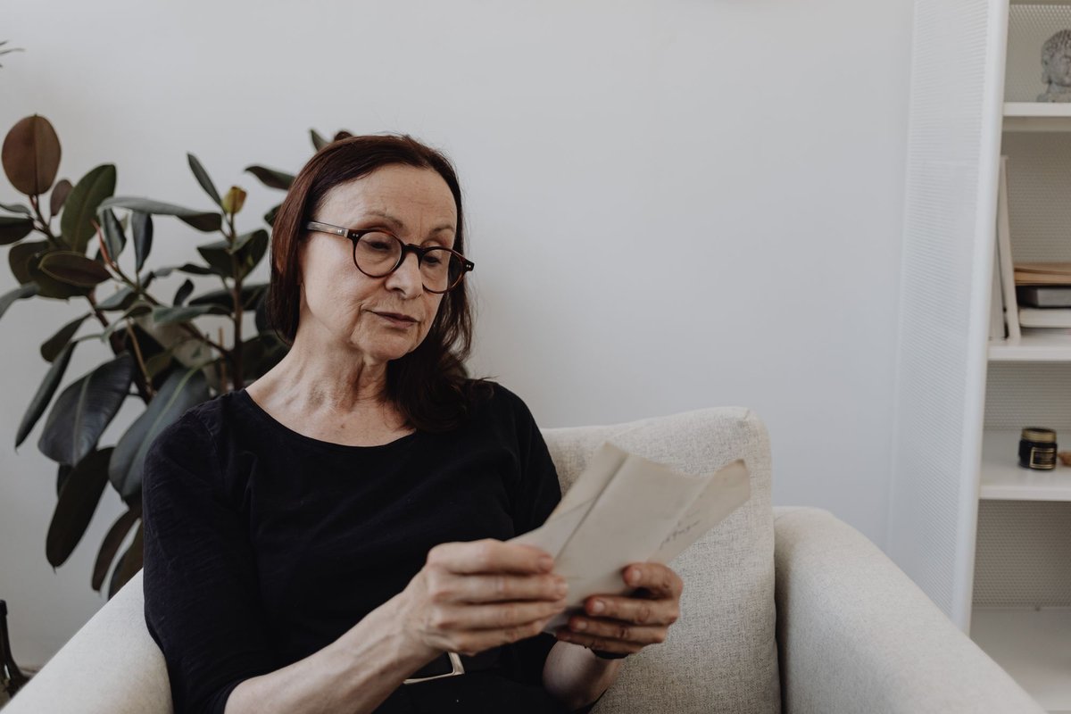 Woman with glasses sitting in an armchair reading a letter at home