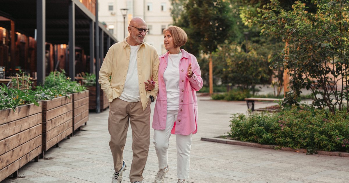 Older couple walking arm in arm along a tree-lined city sidewalk