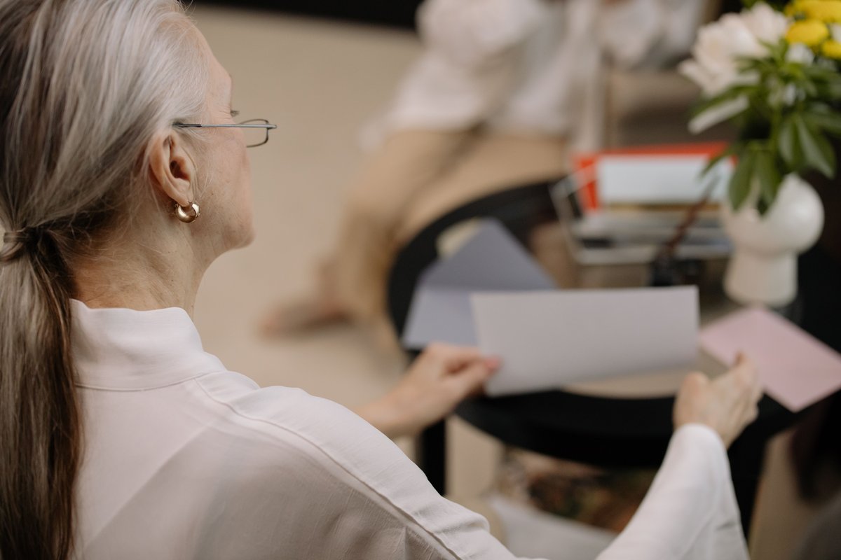 Older woman with gray hair holding papers at a table with flowers while preparing documents
