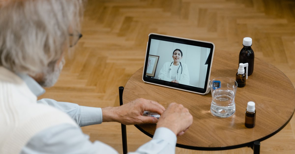 Older man at a table with medicine bottles taking a video visit with a doctor on a tablet