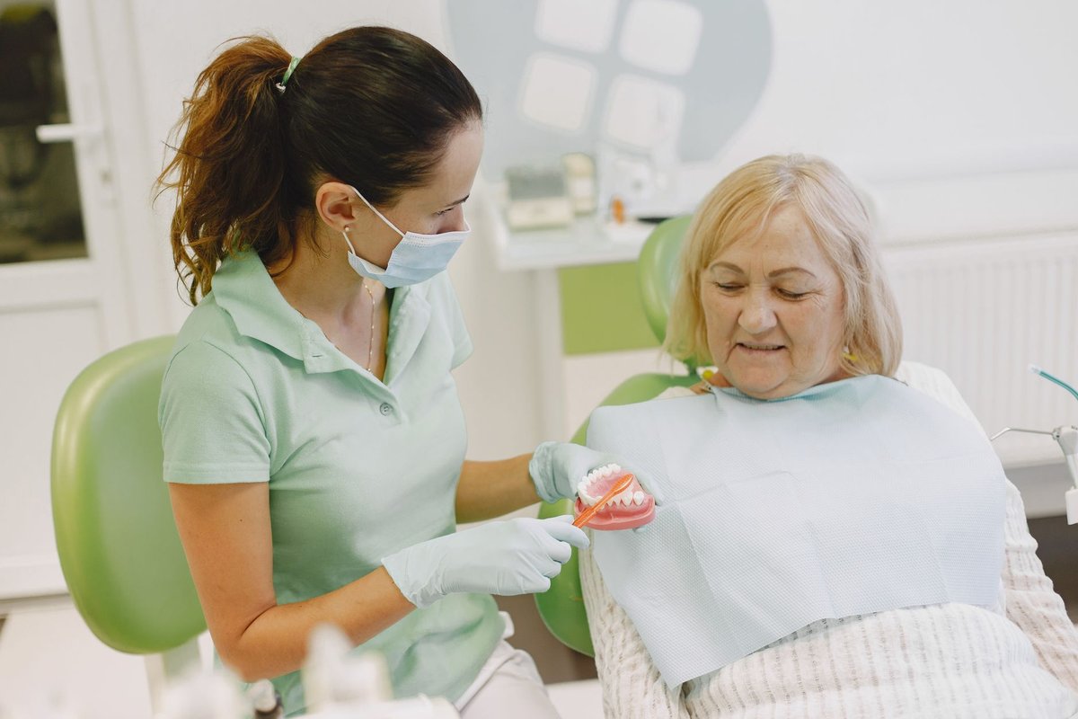 Dental hygienist showing an older woman how to brush with a toothbrush and tooth model