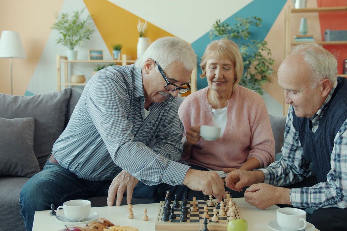 Three older adults enjoying a chess game and tea together in a cozy living room