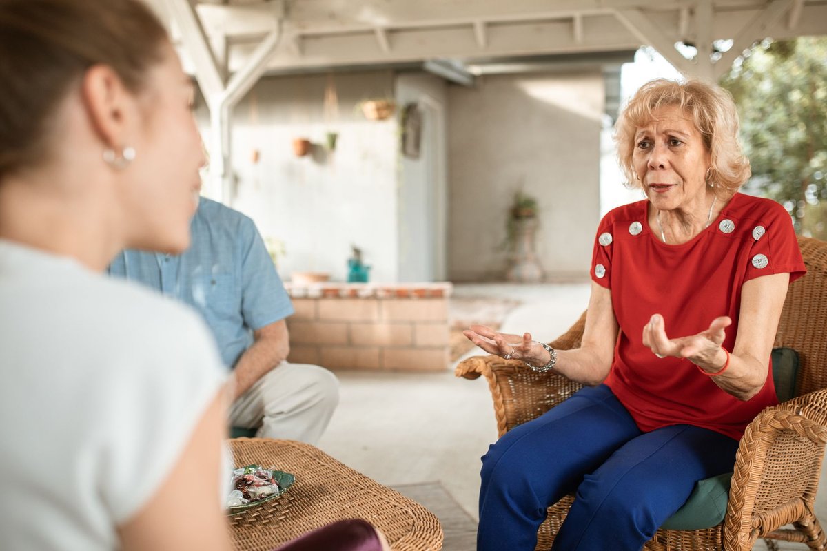 Older woman in a red top talking with a younger woman on a covered patio