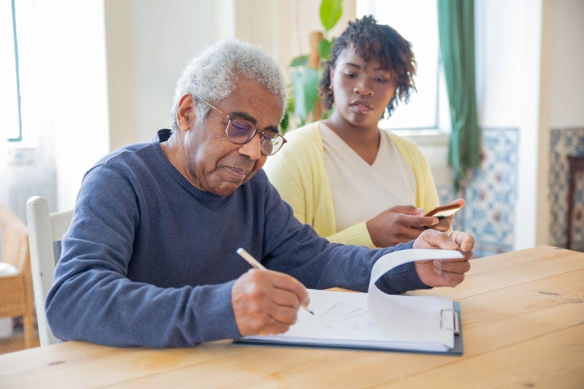 Older man filling out forms at a table while a family member helps with paperwork