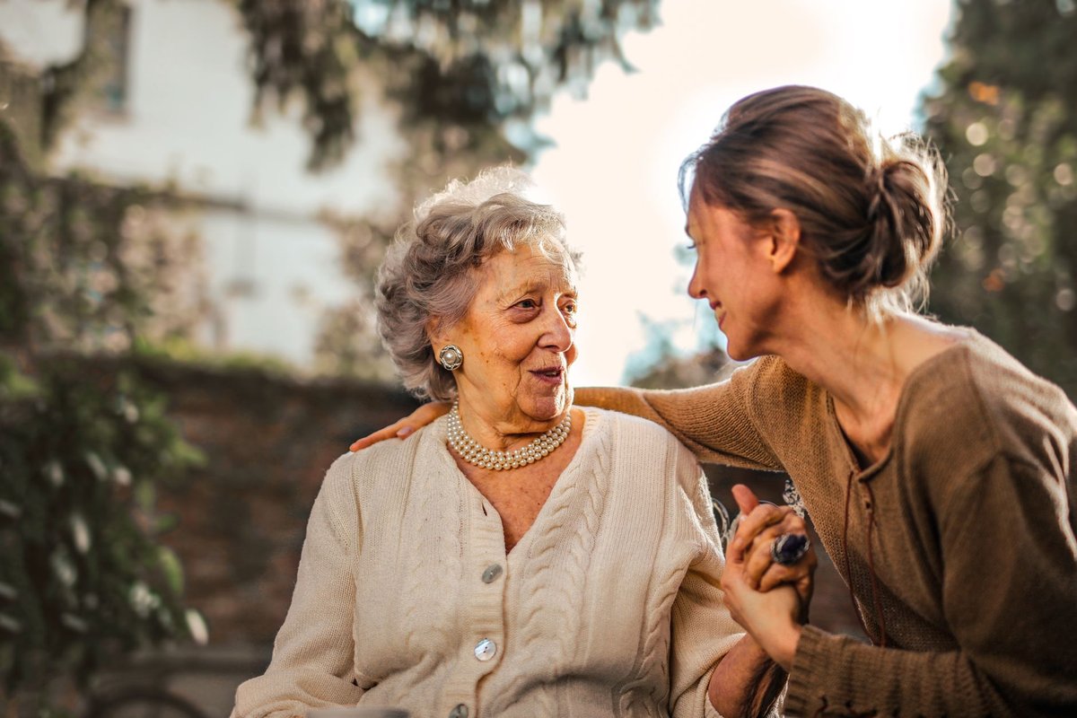 Adult daughter holding her elderly mother's hand, a family caregiver taking time to care for a parent