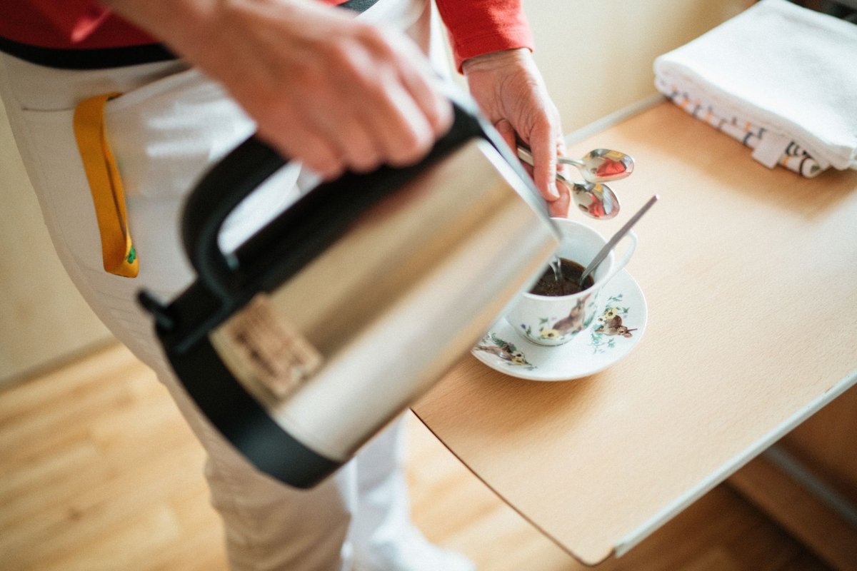 Helper's hands pouring hot tea from a kettle into a cup on a small table