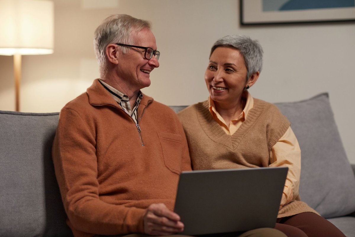 Older couple smiling at each other while looking at a laptop on the sofa