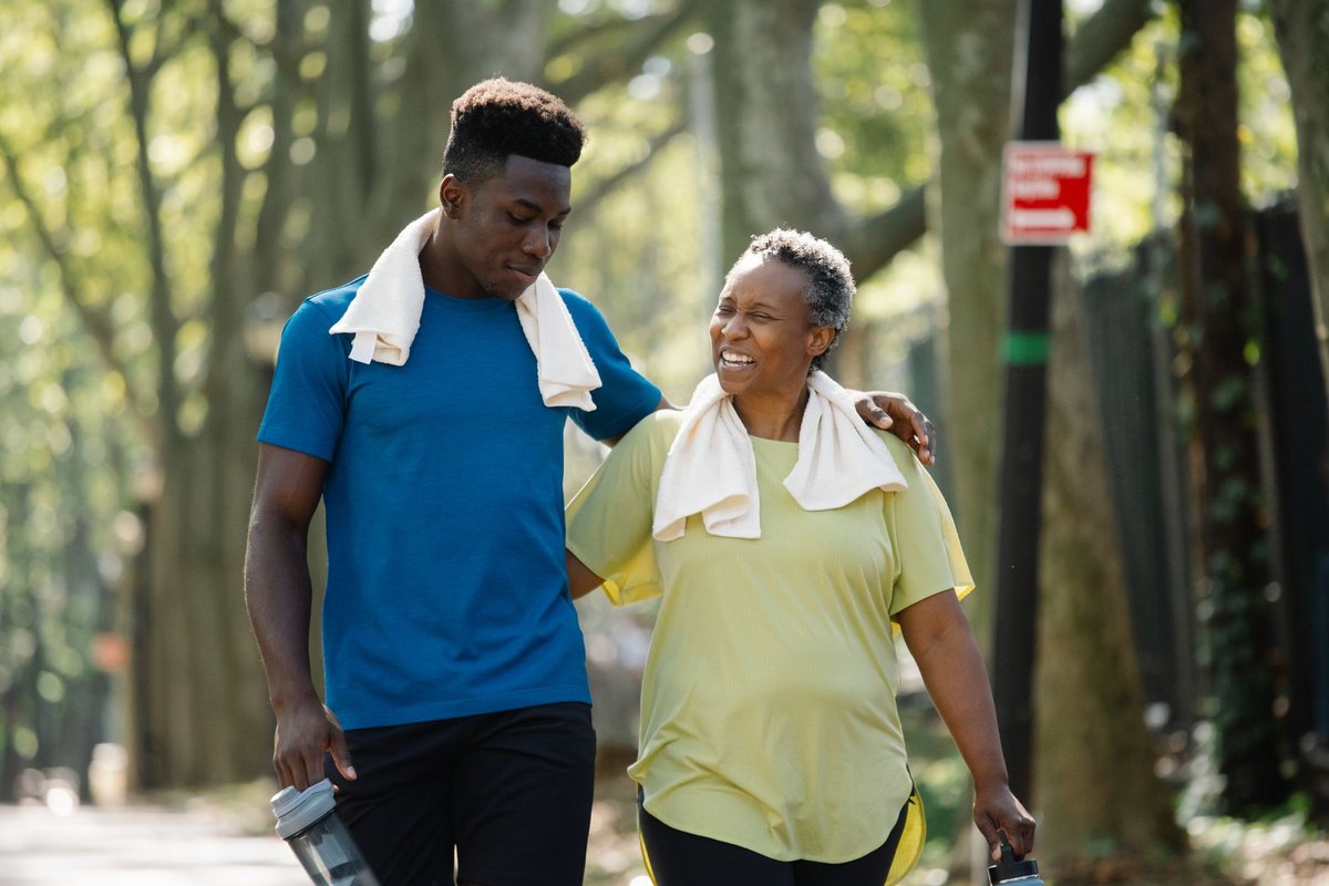 Young man and his mother walking arm in arm along a tree-lined street