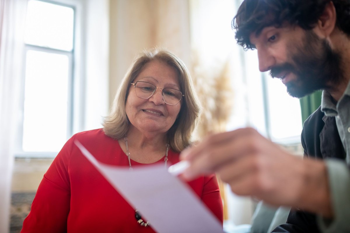 Smiling older woman and a younger man looking over a document together near a window
