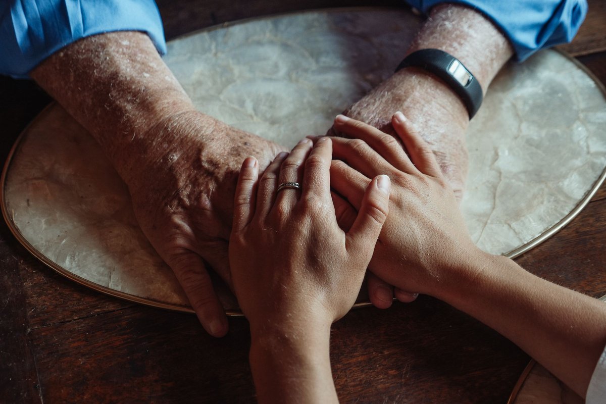 Younger hands resting gently over an older person's hands on a wooden table