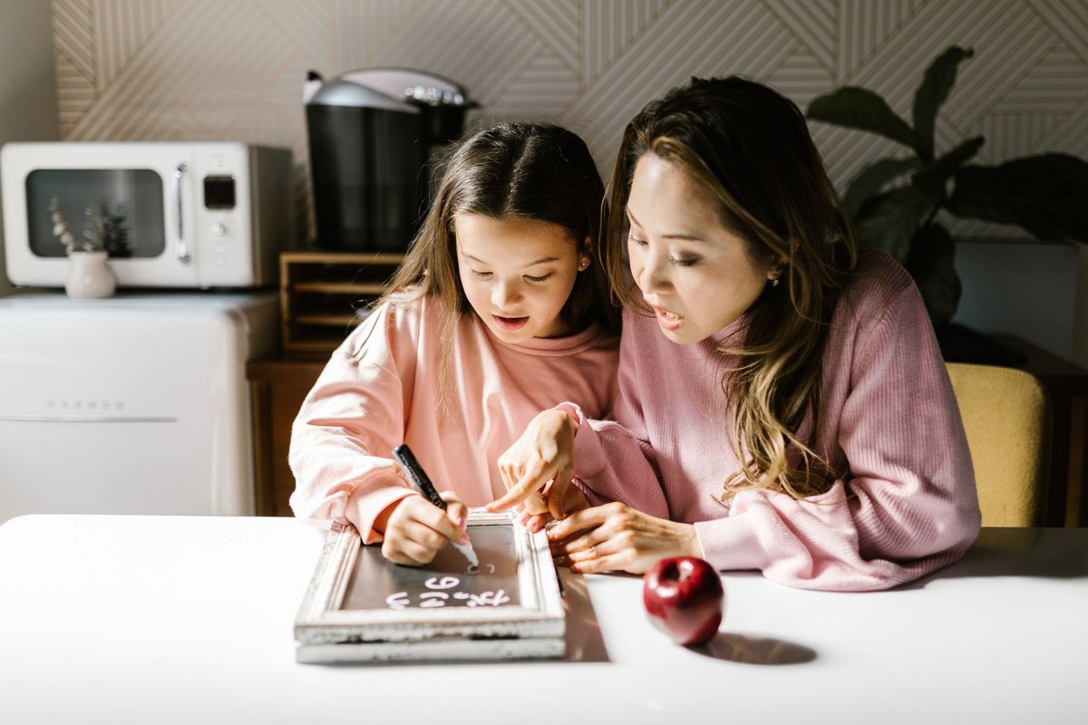 Mother and daughter writing on a small chalkboard together at a kitchen table