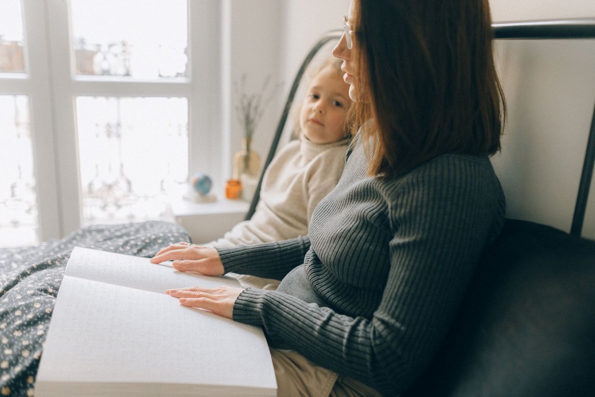 Woman and child reading a braille book together in a bright bedroom